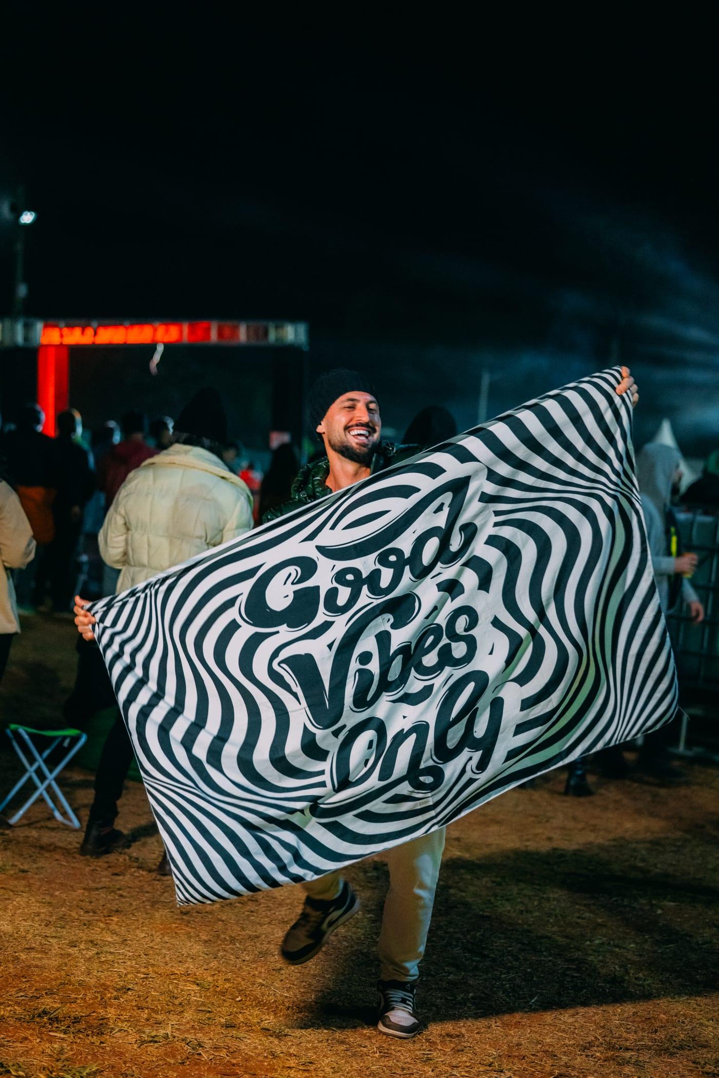 Participante com bandeira Good Vibes Only no STL Valley, transmitindo toda a energia positiva e vibe do festival